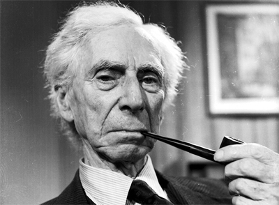 Retrato em preto e branco de um senhor de cabelos brancos segurando um cachimbo na boca e olhando para a câmera em ambiente interno.