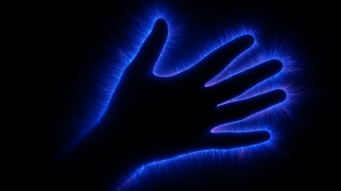 Fotografía de una mano con efecto de descarga eléctrica azul alrededor, capturada mediante la técnica de fotografía Kirlian.