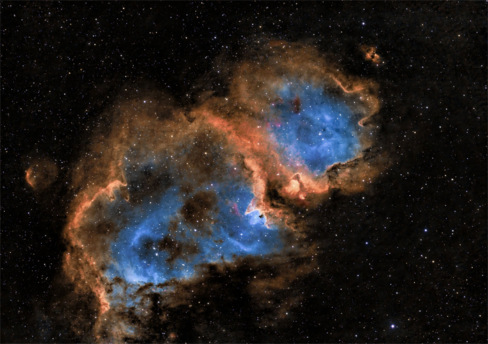 Fotografía astronómica de la Nebulosa del Corazón y el Alma, mostrando nubes de gas interestelar en tonos azules y anaranjados rodeadas de estrellas.