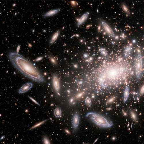 Fotografía astronómica de un cúmulo de galaxias en el universo profundo, mostrando numerosas galaxias espirales y el brillo concentrado en el centro.